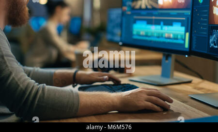 Männliche Videographer Bearbeitungen und Kürzungen Filmmaterial und Sound auf seinem Personal Computer mit zwei Displays. Sein Büro ist moderne und kreative Loft Studio. Stockfoto