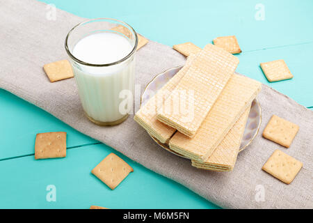 Cracker und Wafer mit Milch stehen auf einer hölzernen blauer Tisch, auf einer Leinwand Serviette. Süßes Mittagessen Stockfoto