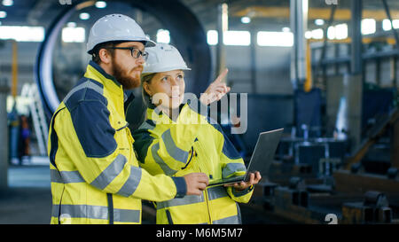 Portrait von Männlichen und Weiblichen Wirtschaftsingenieure in harte Hüte diskutieren Neues Projekt bei der Verwendung von Laptops. Sie Rettungswesten tragen. Sie Arbeiten an der Schwere Stockfoto