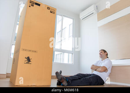 Mann sitzt auf dem Boden in einer leeren Wohnung in einem großen Karton. Man denkt an die große Paket in der neuen Wohnung. Stockfoto