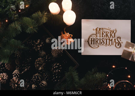 Flach mit Geschenken, Tannenzapfen im Holzkasten, frohe Weihnachten Grußkarte auf schwarz Tischplatte Stockfoto