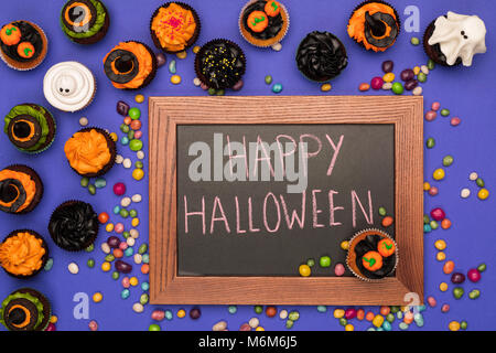 Blick von oben auf die Halloween Cupcakes, Bonbons und Board mit happy halloween Inschrift auf Blau Stockfoto