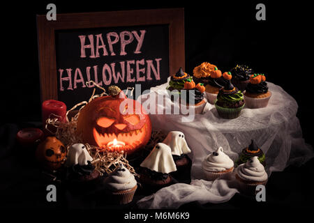 Nahaufnahme der halloween Cupcakes, Tafel mit Inschrift und Happy Halloween Kürbis in der Dunkelheit Stockfoto