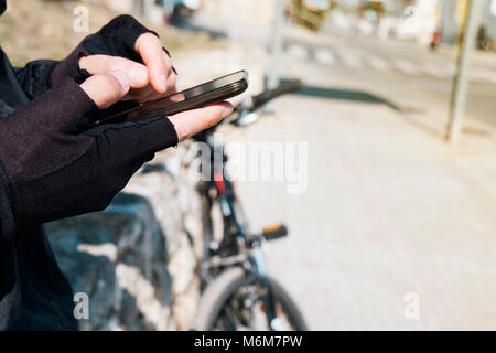 Nahaufnahme eines jungen kaukasischen Radfahrer Mann mit Fahrrad Handschuhe mit seinem Smartphone Neben seinem Fahrrad im Freien Stockfoto