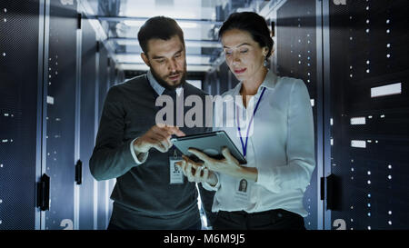 Männliche und Weibliche IT-Ingenieure im Rechenzentrum/Serverraum, Sie sprechen. Einer von ihnen hält Tablet Computer. Stockfoto