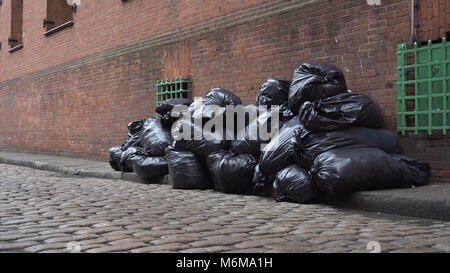 Schwarze Müllsäcke gefüllt mit Müll sitzen auf dem bordstein von Brooklyn, New York Street entlang der Seite ein Backsteingebäude warten gesammelt und entsorgt werden, b Stockfoto