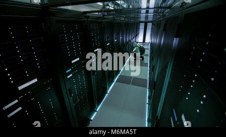 Sicherheit Kamera Ansicht einer Hooded Hacker im Data Center, mit seinem Laptop wie er zu einem Der Rack-server, begeht Verbrechen verbindet. Stockfoto