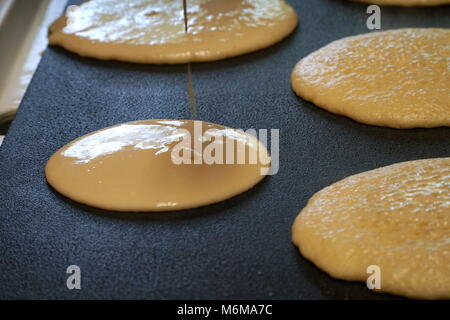 Pfannkuchenteig Backmischung aus einer Schüssel auf einen heißen elektrische Grillpfanne Küche leckere Frühstück Mahlzeit für eine Familie gegossen. Stockfoto