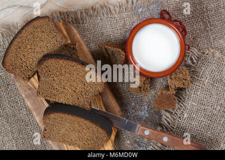 Milch in einem rustikalen Ton Glas mit Roggen Brot auf einem Sack Stockfoto