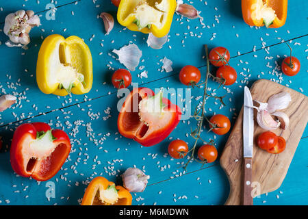 Zutaten: frische Paprika, roher Reis und Knoblauchzehen auf einem cyan Holzoberfläche Reis Mehl in eine olivenholz Platte auf einem Sack. Stockfoto