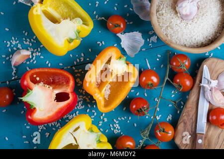 Zutaten: frische Paprika, roher Reis und Knoblauchzehen auf einem cyan Holzoberfläche Reis Mehl in eine olivenholz Platte auf einem Sack. Stockfoto