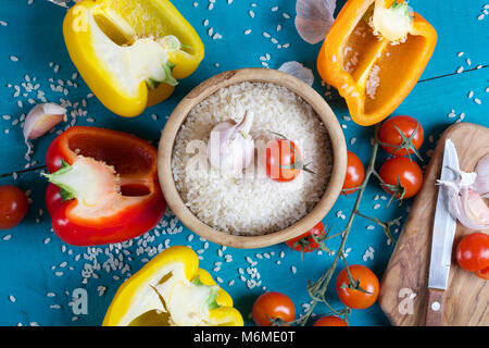 Zutaten: frische Paprika, roher Reis und Knoblauchzehen auf einem cyan Holzoberfläche Reis Mehl in eine olivenholz Platte auf einem Sack. Stockfoto