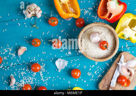 Zutaten: frische Paprika, roher Reis und Knoblauchzehen auf einem cyan Holzoberfläche Reis Mehl in eine olivenholz Platte auf einem Sack. Stockfoto