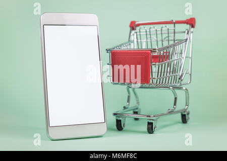 Warenkorb Miniatur- und leerer Bildschirm Smartphone auf grünem Hintergrund. Online shopping e-commerce Konzept Stockfoto