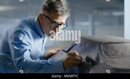 Professional Automotive Designer mit Rechen formt futuristischen Auto Modell aus Plastilin Ton. Er arbeitet in einem speziellen Studio In einer Autofabrik entfernt Stockfoto