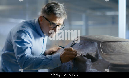 Professional Automotive Designer mit Rechen formt futuristischen Auto Modell aus Plastilin Ton. Er arbeitet in einem speziellen Studio In einer Autofabrik entfernt Stockfoto