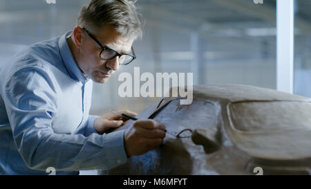 Professional Automotive Designer mit Rechen formt futuristischen Auto Modell aus Plastilin Ton. Er arbeitet in einem speziellen Studio In einer Autofabrik entfernt Stockfoto