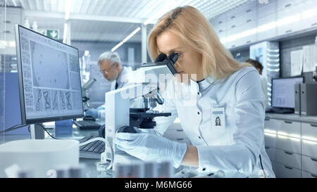 Weibliche Wissenschaftler befasst sich mit biologischen Proben unter dem Mikroskop. Sie und Ihre Kollegen arbeiten in einem großen modernen Labor/Medical Center. Stockfoto