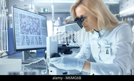 Weibliche Wissenschaftler befasst sich mit biologischen Proben unter dem Mikroskop. Sie und Ihre Kollegen arbeiten in einem großen modernen Labor/Medical Center. Stockfoto