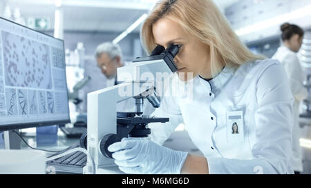 Weibliche Wissenschaftler befasst sich mit biologischen Proben unter dem Mikroskop. Sie und Ihre Kollegen arbeiten in einem großen modernen Labor/Medical Center. Stockfoto