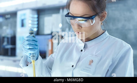 Weibliche Wissenschaftler verwendet Mikropipette Füllung Röhrchen in einem großen modernen Labor. Im Hintergrund arbeiten die Wissenschaftler im Computer. Stockfoto