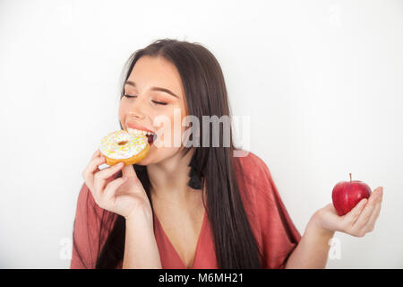 Hübsches junges Mädchen nimmt einen Bissen von einem Donut und mit einem Apfel in der Hand. Stockfoto