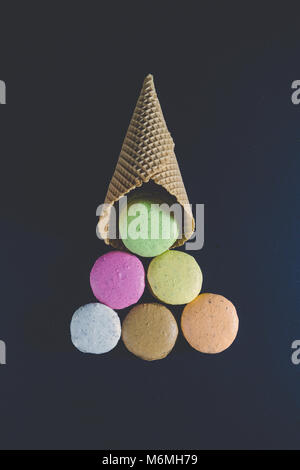 Bunte macarons Cookies und Waffel Kegel in Form von Eis Kugeln Weihnachtsbaum auf schwarzen Hintergrund. Minimalen Begriff Stockfoto