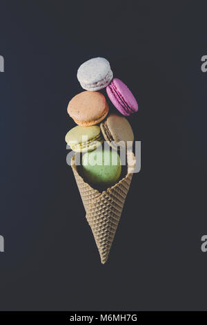 Bunte macarons Cookies im Waffle Kegel in Form von Eis Kugeln auf schwarzem Hintergrund. Minimalen Begriff Stockfoto