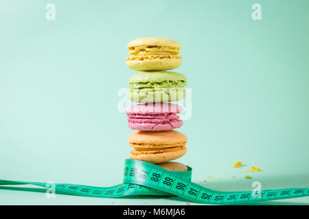 Gestapelte bunte Macarons mit weichen Maßband um sie gebunden isoliert auf grünem Hintergrund. Minimale gesunde Lebensweise und Ernährung Konzepte. Stockfoto