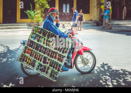 Ein Händler ein grosses Board von Sonnenbrillen auf einem Moped auf der Straße in Hoi An, Vietnam Stockfoto