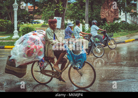 Menschen auf Mopeds und Fahrräder Transport von Passagieren und Waren durch die verregneten Straßen von Siem Reap Stockfoto