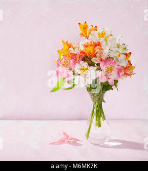 Blumenstrauß von Alstroemeria in einem durchsichtigen Glas Vase auf rosa Hintergrund Stockfoto