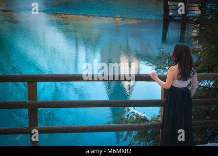 Zurück Blick auf eine Brünette junge Frau, elegant in einen langen schwarzen Rock gekleidet, bewundern Sie das blaue Wasser der Blautopf Frühling, in Blaubeuren, Deutschland. Stockfoto