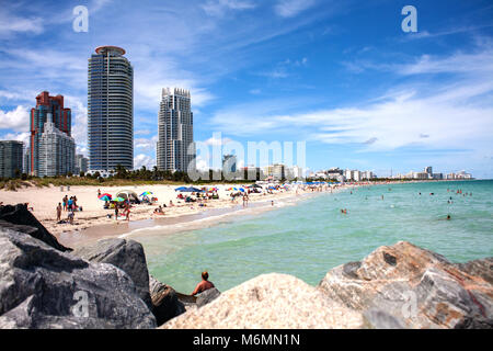 Blick auf Miami South Beach über Felsen während der sonnigen Tag. Hotels und luxuriösen Apartments im Hintergrund. Leute Chillen am Sandstrand. Stockfoto