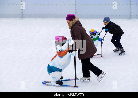 Frau und Kind Spaß skatimg auf eine Öffentliche Eisbahn über einen Rahmen für die Unterstützung. Karlsplatz, München, Bayern, Deutschland, Europa Stockfoto