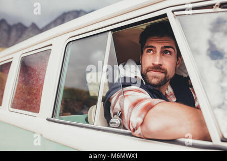 Hübscher Kerl mit einem Van und suchen vor dem Fenster. Mann auf einem Road Trip durch alte minivan reisen. Stockfoto