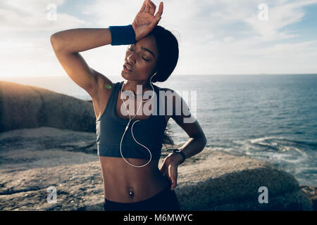 Fitness Frau auf der Suche nach intensiven körperlichen Training müde. Sportlerin stehen über die Felsen am Strand mit der Hand auf den Kopf. Stockfoto