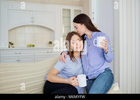 Zwei Freundinnen mit Tassen in der Hand auf einer Sitzung in einem Zimmer in der Küche. Stockfoto