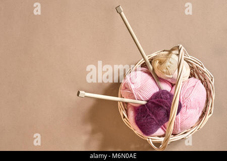 Garn Kugeln. Kugeln aus farbigen Garnen in einem Korb Schale. Garne zum Stricken auf einem beigen Hintergrund. Stricken als eine Art von Handarbeit. Stricknadeln und Multi-farbigen Garnen Blick hell. Stockfoto