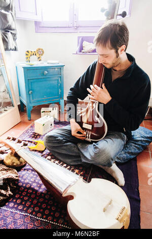 Junge Mann spielt klassische indische Musik auf einer Sarod zu Hause im Stadtteil Albaicin Granada, Andalusien, Spanien. Stockfoto