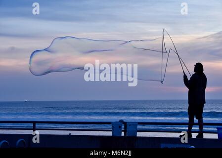 Männliche Schauspieler, groß, große Seifenblasen bei Sonnenuntergang mit Blick auf den Pazifik, Pacific Beach, San Diego, Kalifornien, USA. Stockfoto