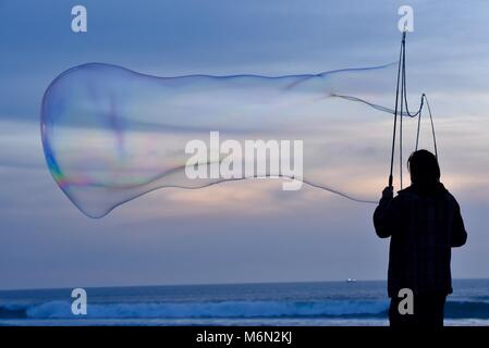 Männliche Schauspieler, groß, große Seifenblasen bei Sonnenuntergang mit Blick auf den Pazifik, Pacific Beach, San Diego, Kalifornien, USA. Stockfoto