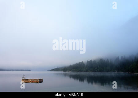 Panorama von misty Gletschersee Bohinj mit holzfloß Schwimmen mit Leiter schwimmend auf einem See, Nationalpark Triglav, Julische Alpen, Gorenjska, Slowenien Stockfoto