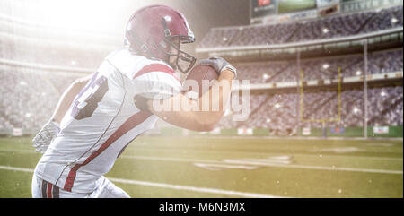 American Football Spieler läuft mit dem Ball auf grossen modernen Stadion Feld mit Lichtern und Fackeln isoliert Stockfoto