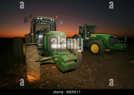 , Slawonien Osijek/Kroatien - 1/25/2018: zwei Traktoren von John Deere in einem Feld mit Sonnenuntergang und schönen Himmel im Hintergrund Stockfoto