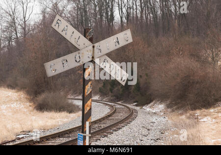 Eine Rail Road Kreuzung Zeichen steht an der Seite eine Kurve in RR-Titel. Beide zeigen ihr Alter von Jahren und Jahren der Verwitterung. Stockfoto