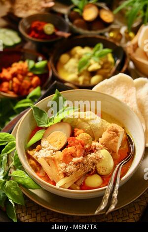 Lontong Cap klicken Sie meh. Die Javanese-Peranakan Reis Kuchen Suppe mit Hähnchen Curry, Chayote Squash Curry Soja, Ei, Garnelen Eintopf, Boden Soja- und Cracker. Stockfoto