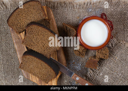 Milch in einem rustikalen Ton Glas mit Roggen Brot auf einem Sack Stockfoto