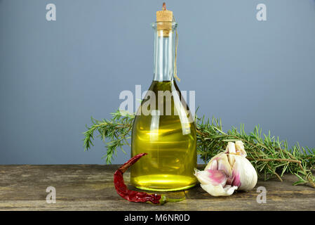 Die Flasche auf dem Tisch enthält natives Olivenöl extra in Italien produziert. Chili, Knoblauch und Rosmarin sind die aromatischen Kräuter Stockfoto