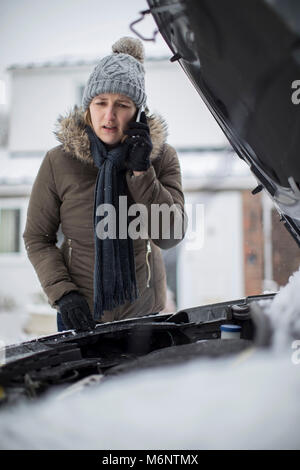 Weibliche Autofahrer Aufgeschlüsselt im Schnee für Pannenhilfe auf Handy Stockfoto